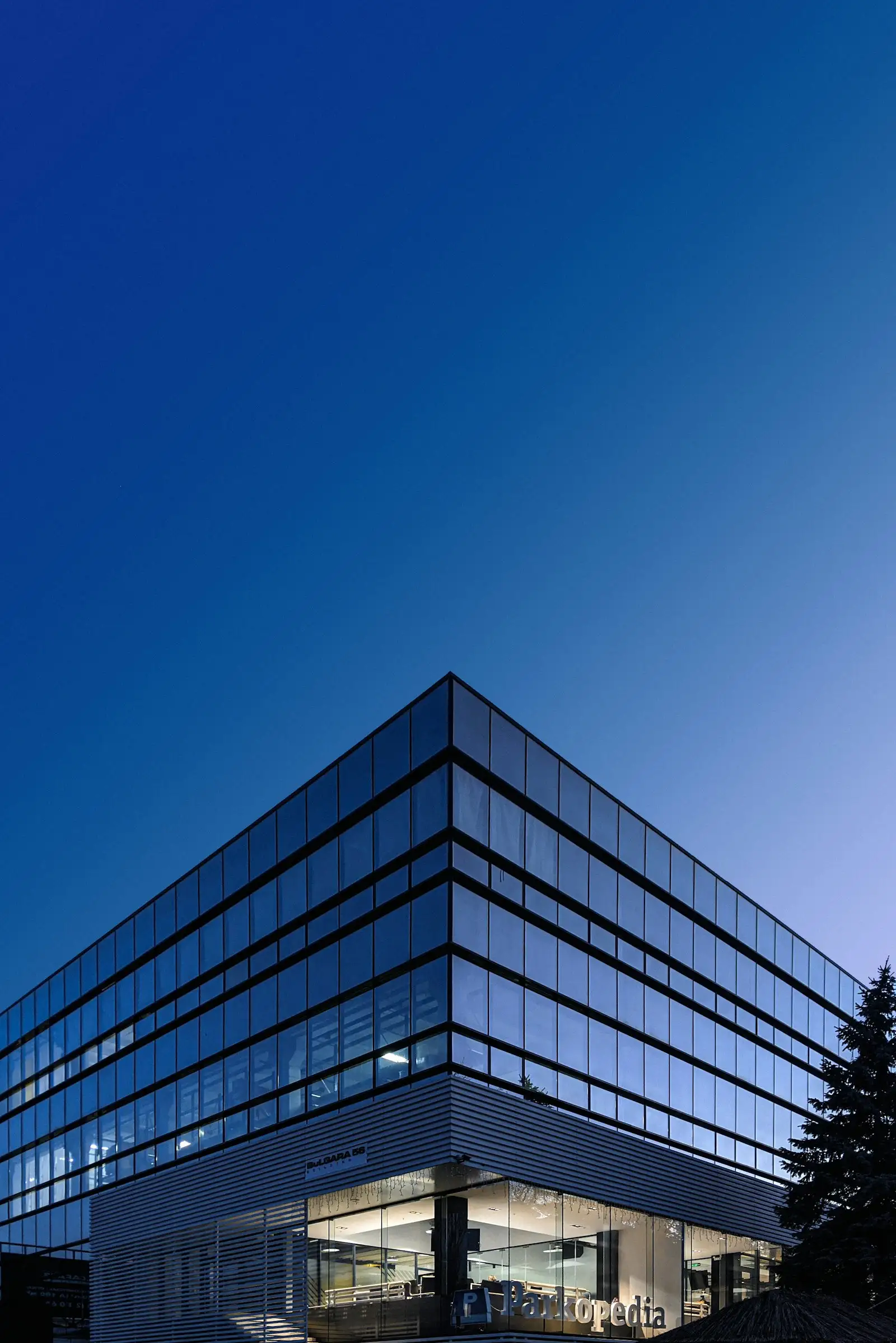 Corner of a glass office building against a deep blue sky