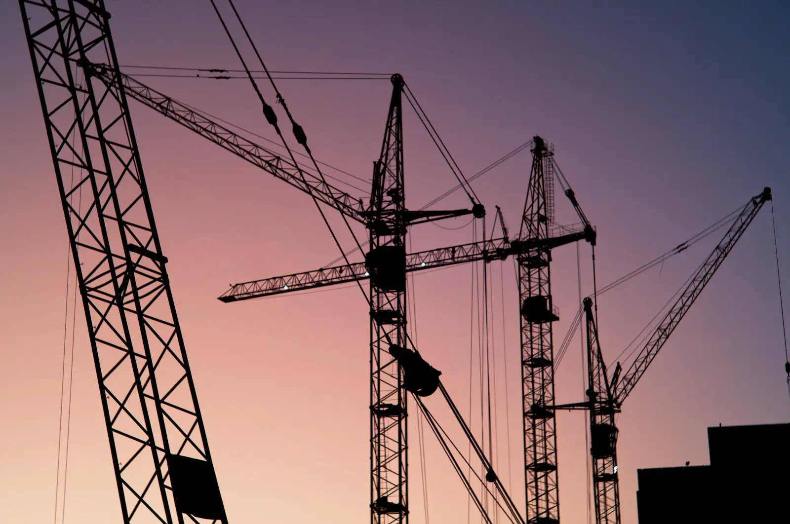 Silhouetted tower cranes against a dusk sky